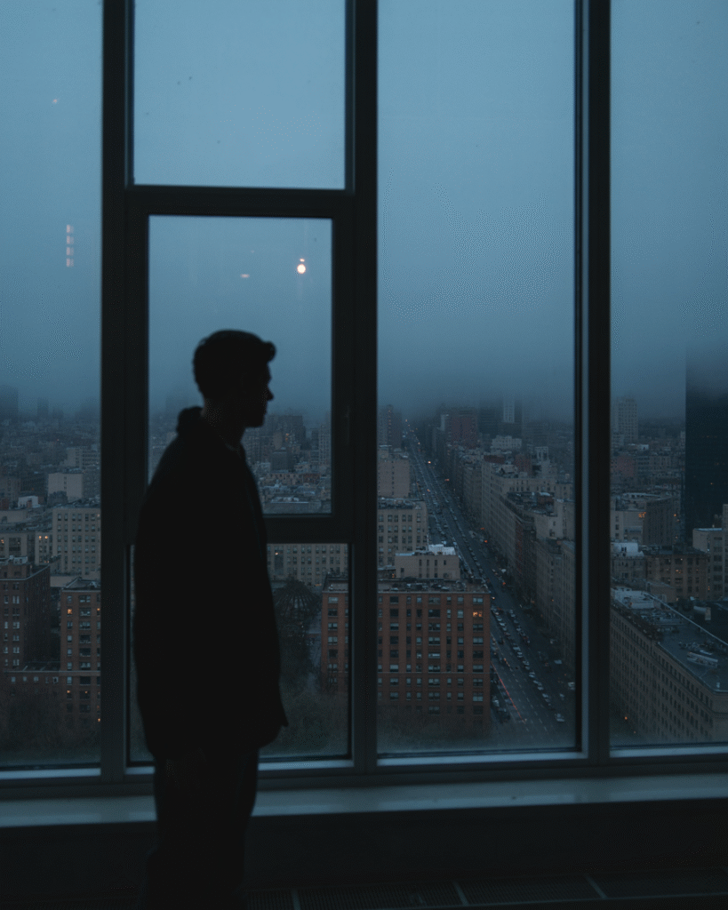 Person looking out window at cityscape with muted colors, representing feeling stuck or misaligned with location